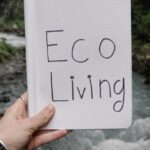 Sustainable Living - Person Holding a Notebook with a Text "Eco Living" on the Background of a River in a Forest